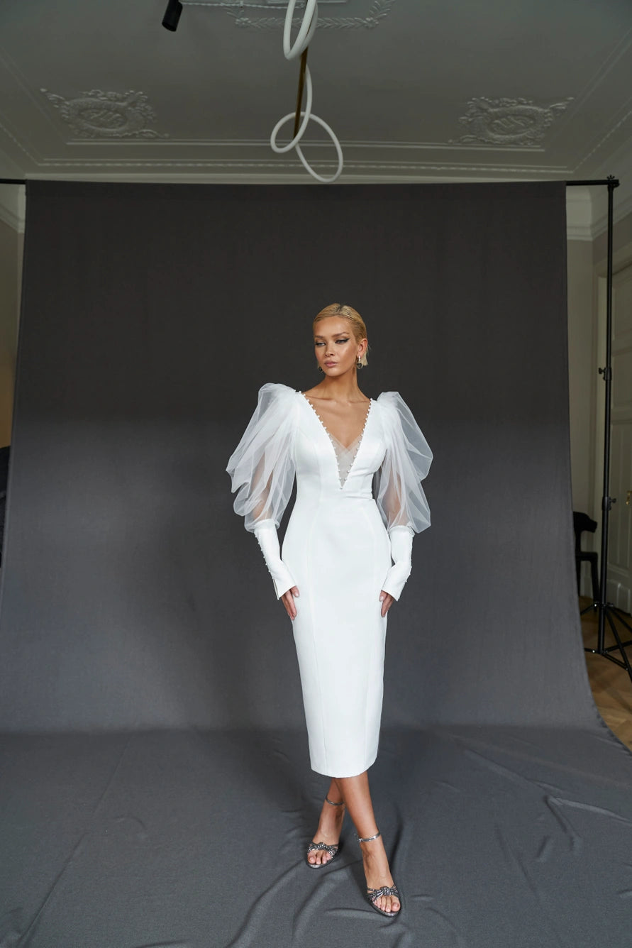 Formez une robe de mariée midi ajustée avec de longues manches bouffantes et un décolleté en V. Fermeture à glissière basée.