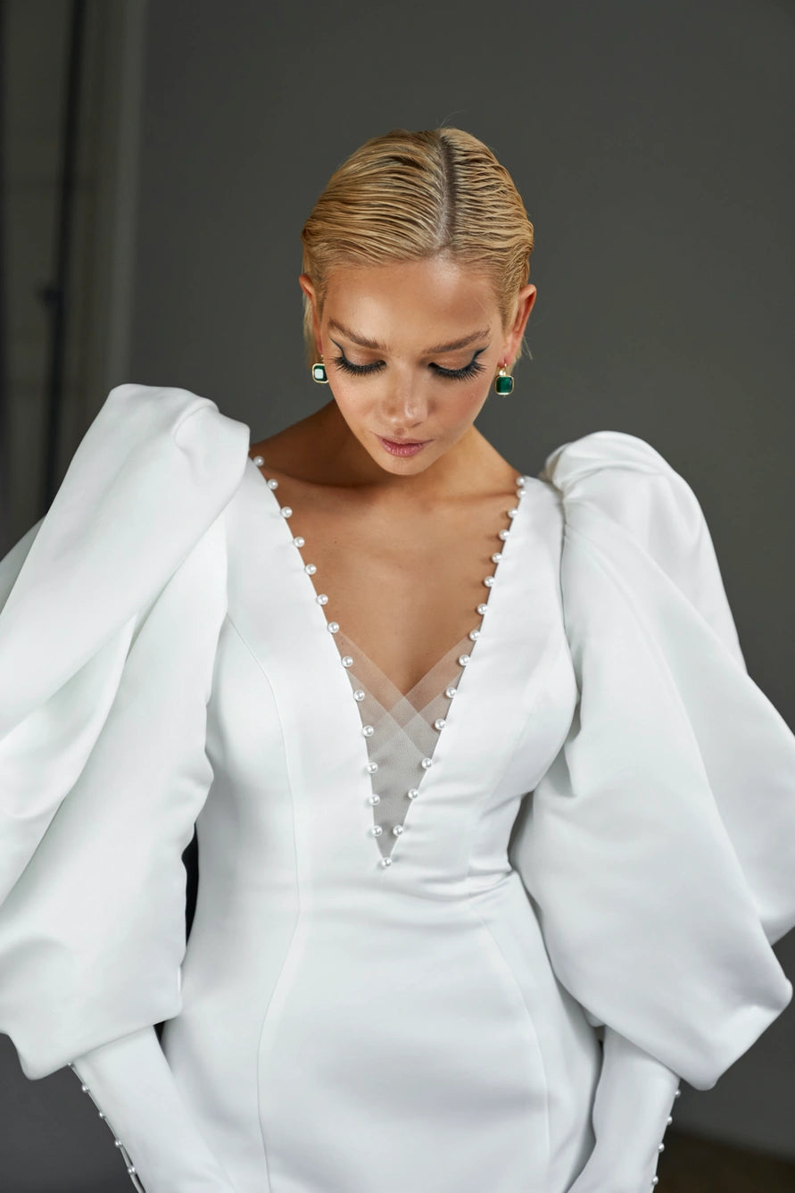 Form fitting short wedding dress with long puff sleeves and V-shaped neckline. Low back zipper.