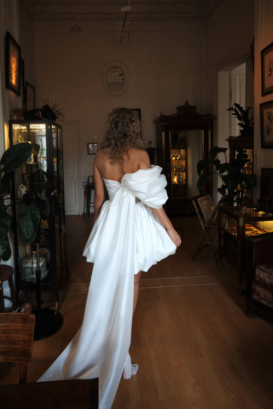 Robe de mariée courte avec de longues manches bouffantes et un dos ouvert avec une fermeture éclair.