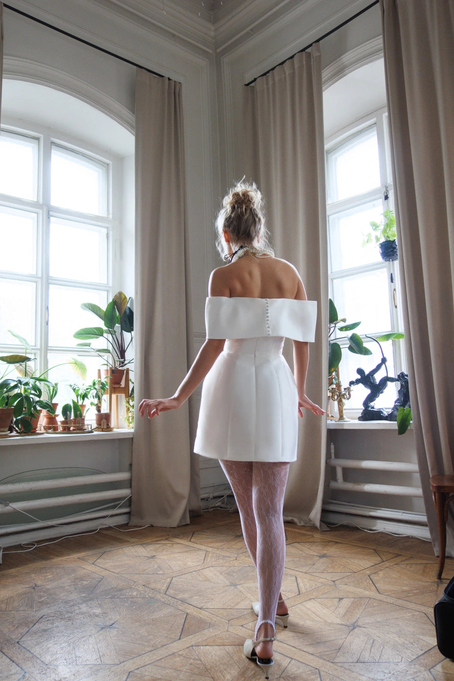 Robe de mariée courte avec de longues manches bouffantes et un dos ouvert avec une fermeture éclair.